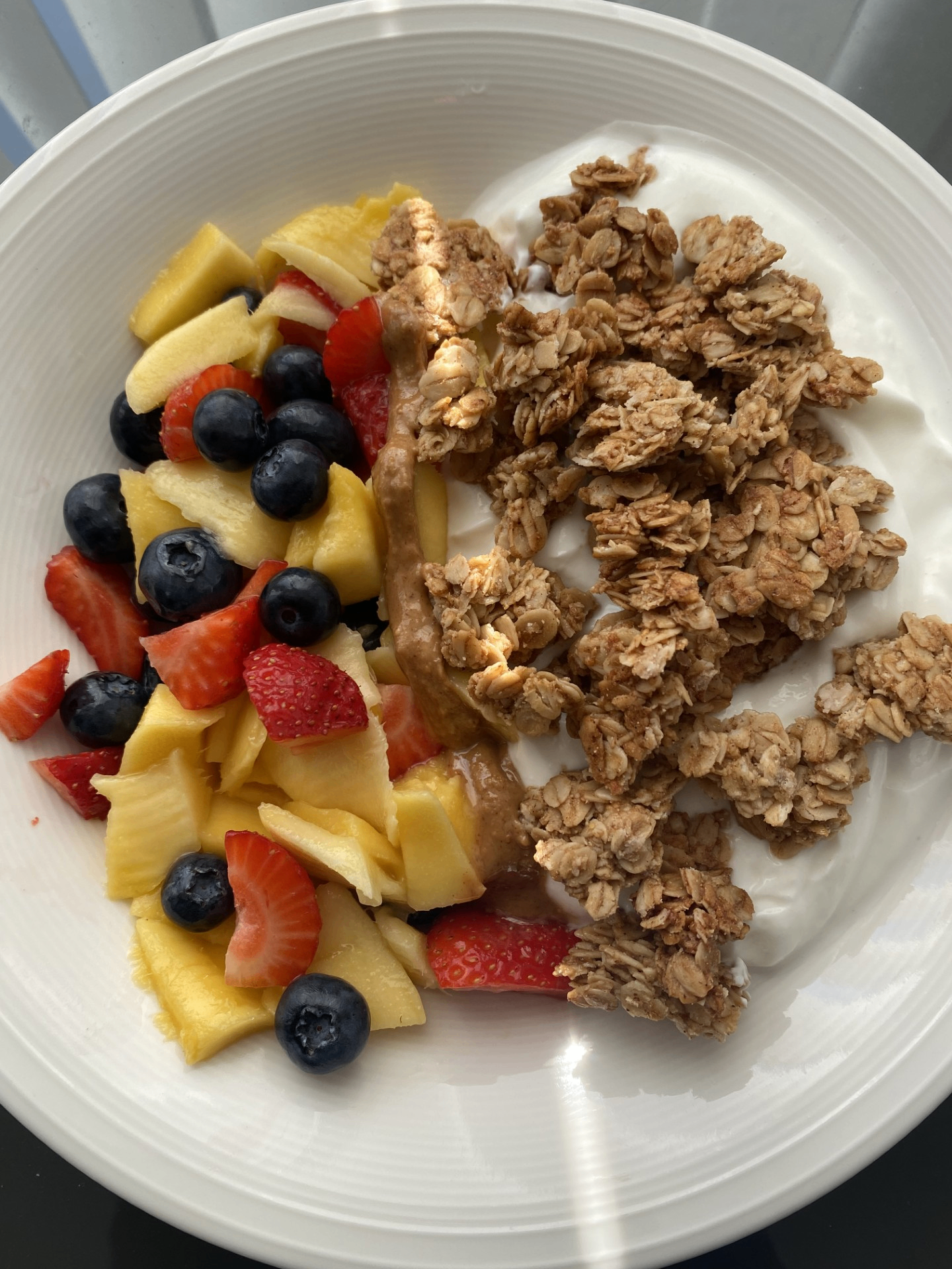 Yogurt bowl with fresh mango, strawberries, blueberries, peanut butter and granola
